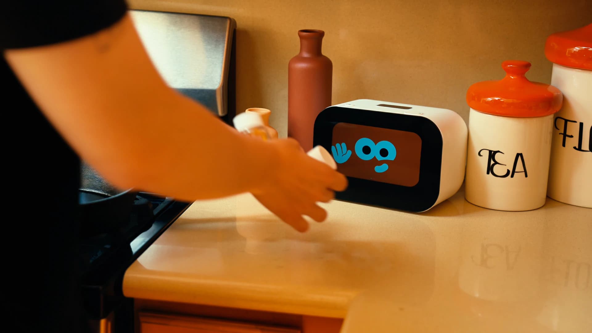 Child reaching toward the Rhem AI health robot on a kitchen counter as it shows a friendly waving face.