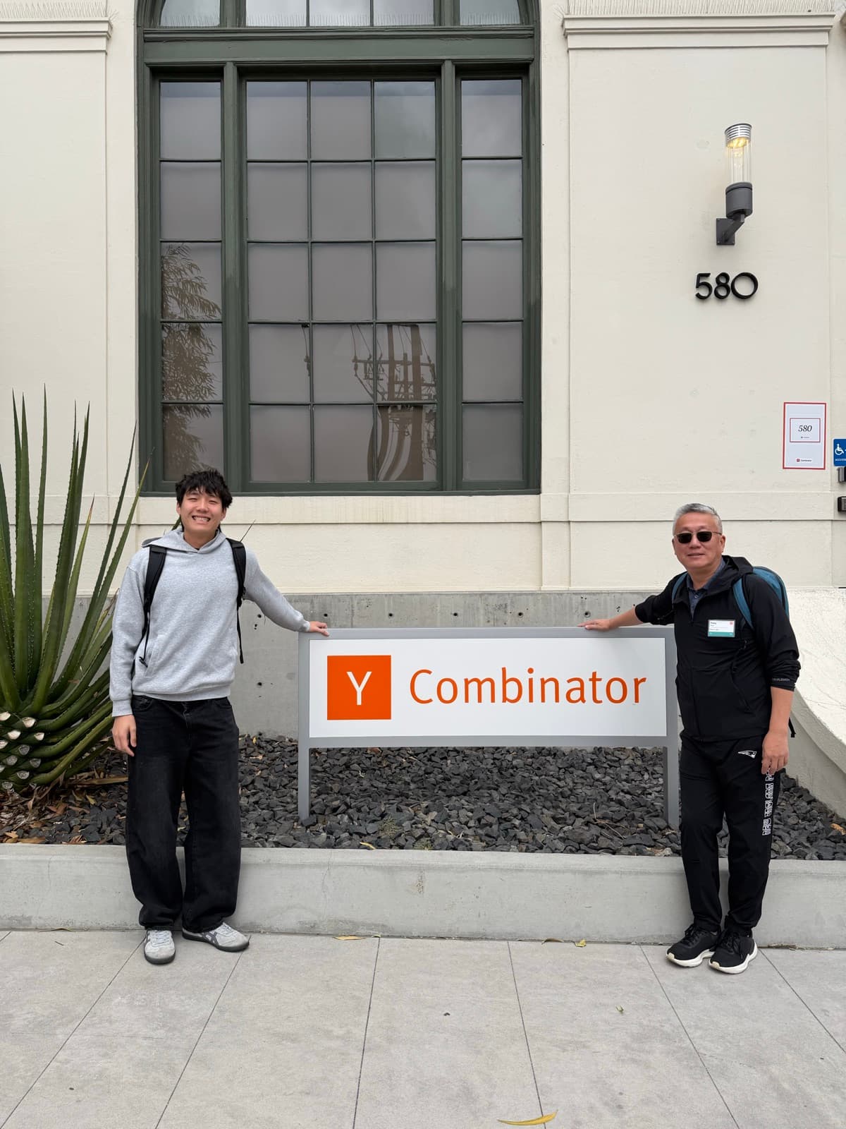 雅各布和休伊在 Y Combinator 標誌旁邊微笑。